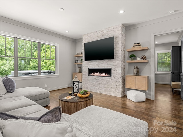 living room featuring a stone fireplace, built in shelves, ornamental molding, and dark hardwood / wood-style floors