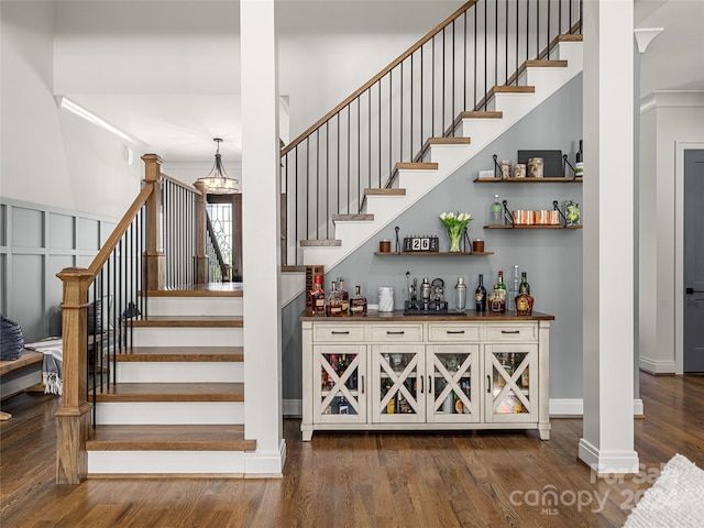 stairs featuring a chandelier, wood-type flooring, bar, and ornamental molding