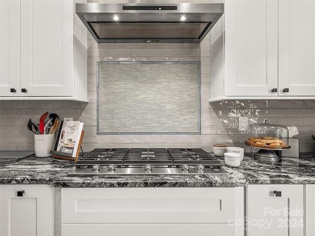 kitchen with dark stone countertops, white cabinetry, backsplash, and exhaust hood