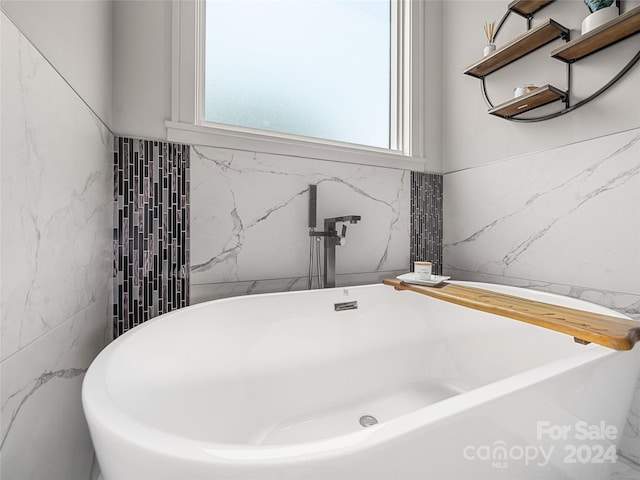 bathroom with plenty of natural light, a bathing tub, and tile walls