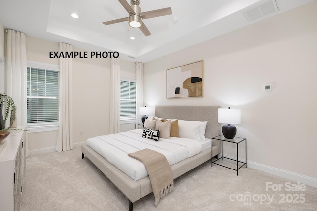 bedroom with a raised ceiling, multiple windows, ceiling fan, and light colored carpet