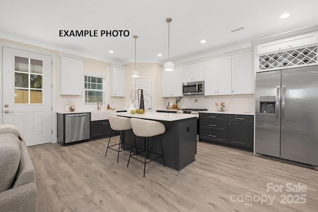 kitchen featuring hanging light fixtures, light wood-type flooring, a kitchen island, white cabinetry, and stainless steel appliances