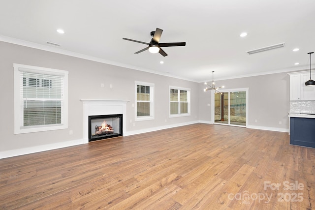 unfurnished living room with crown molding, ceiling fan with notable chandelier, and light wood-type flooring