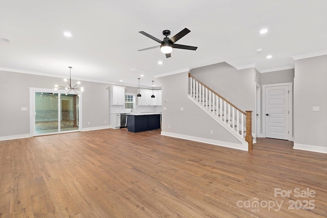 unfurnished living room with ceiling fan with notable chandelier, hardwood / wood-style flooring, and crown molding