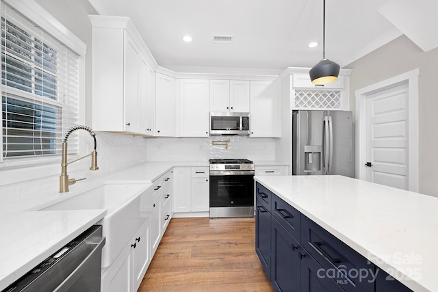 kitchen with blue cabinetry, backsplash, decorative light fixtures, white cabinets, and appliances with stainless steel finishes