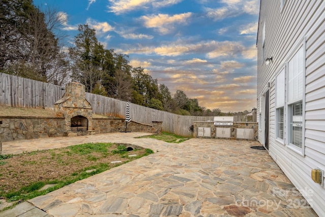 patio terrace at dusk featuring an outdoor stone fireplace, area for grilling, and grilling area