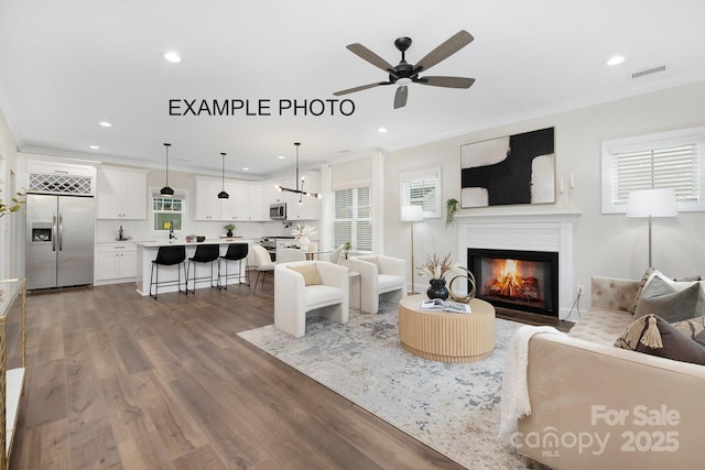 living room with a wealth of natural light, ceiling fan, wood-type flooring, and ornamental molding