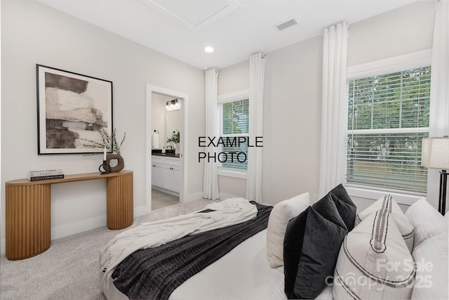 carpeted bedroom with ensuite bathroom and multiple windows