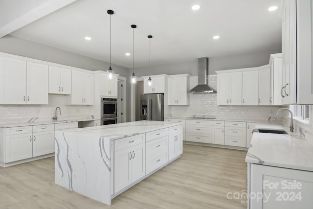 kitchen featuring a center island, wall chimney exhaust hood, white cabinetry, appliances with stainless steel finishes, and decorative light fixtures