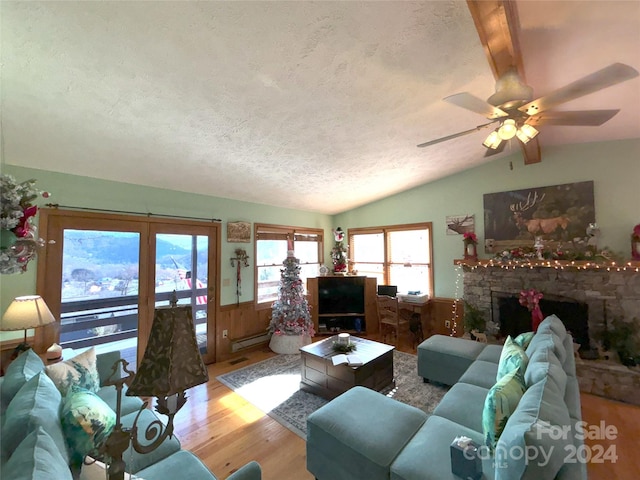 living room featuring light hardwood / wood-style floors, ceiling fan, a textured ceiling, a fireplace, and lofted ceiling with beams