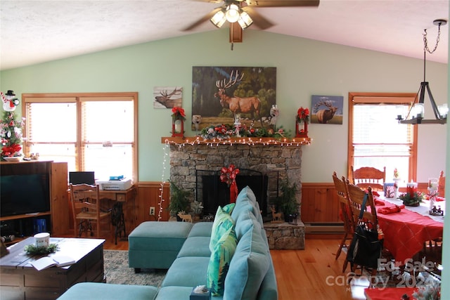 living room with wood-type flooring, a stone fireplace, a baseboard radiator, lofted ceiling, and ceiling fan