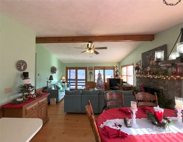 dining space featuring hardwood / wood-style flooring, ceiling fan, a textured ceiling, a stone fireplace, and lofted ceiling with beams