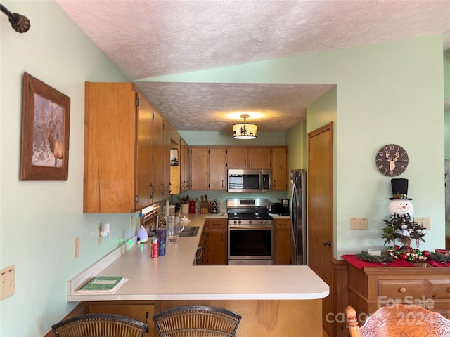 kitchen with stainless steel appliances, a textured ceiling, a kitchen breakfast bar, kitchen peninsula, and lofted ceiling