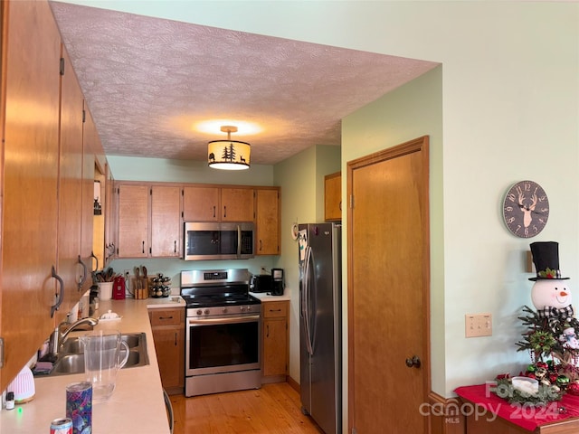 kitchen with light wood-type flooring, appliances with stainless steel finishes, a textured ceiling, and sink