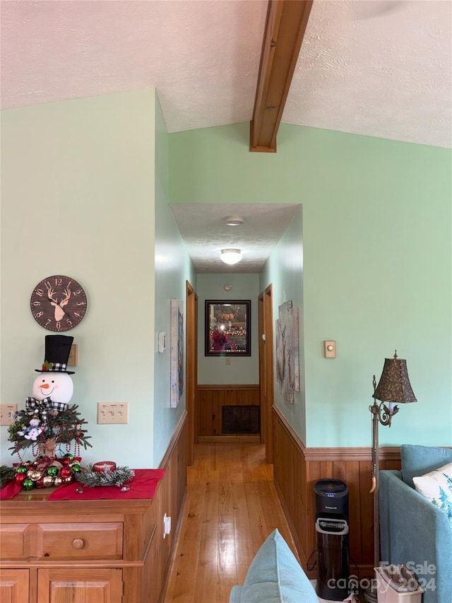 hall with a textured ceiling, lofted ceiling with beams, wooden walls, and light wood-type flooring