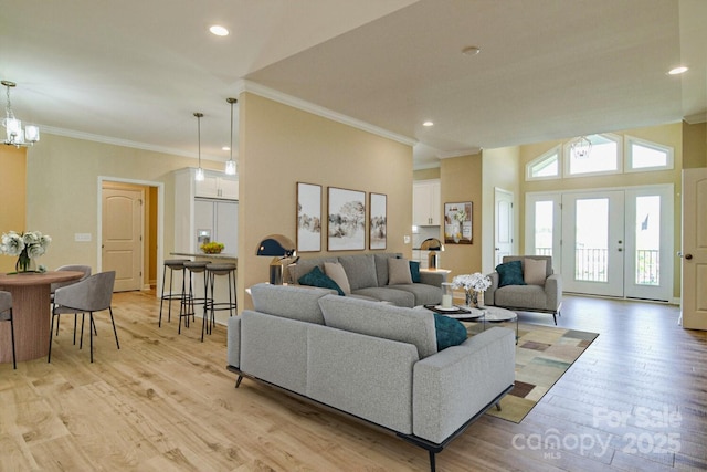 living room with crown molding, an inviting chandelier, lofted ceiling, and light wood-type flooring