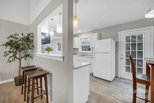 kitchen featuring white refrigerator, a breakfast bar area, light stone countertops, white cabinetry, and light hardwood / wood-style flooring