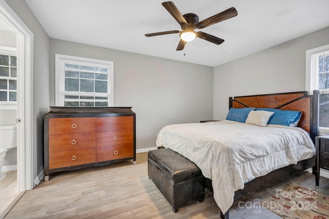 bedroom featuring ensuite bath, ceiling fan, multiple windows, and light wood-type flooring