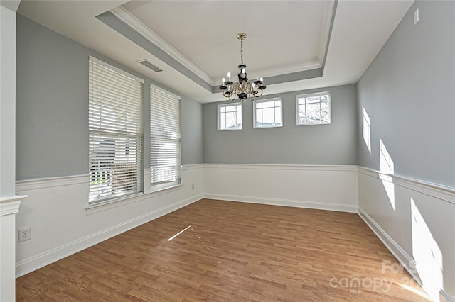 empty room featuring a tray ceiling, crown molding, a chandelier, and light hardwood / wood-style floors