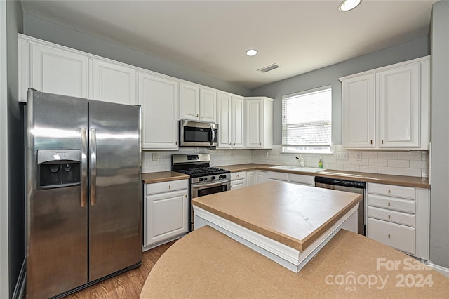 kitchen featuring white cabinetry, sink, stainless steel appliances, light hardwood / wood-style floors, and decorative backsplash