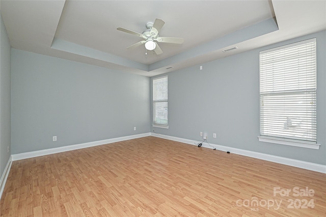 spare room with light hardwood / wood-style floors, a raised ceiling, and ceiling fan