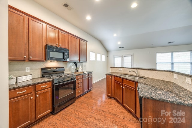 kitchen with wood-type flooring, dark stone countertops, black appliances, and lofted ceiling