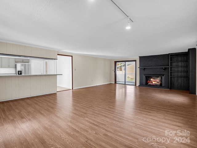 unfurnished living room with a fireplace, light hardwood / wood-style floors, a textured ceiling, and track lighting