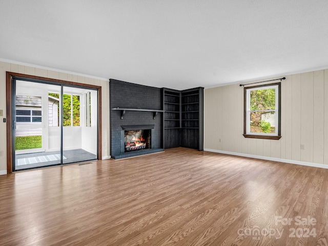 unfurnished living room featuring light hardwood / wood-style floors, crown molding, a healthy amount of sunlight, and a brick fireplace