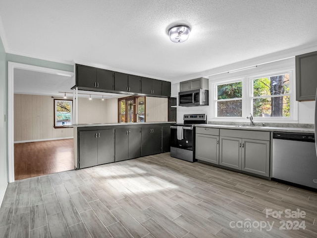 kitchen featuring stainless steel appliances, light wood-type flooring, gray cabinets, wooden walls, and sink