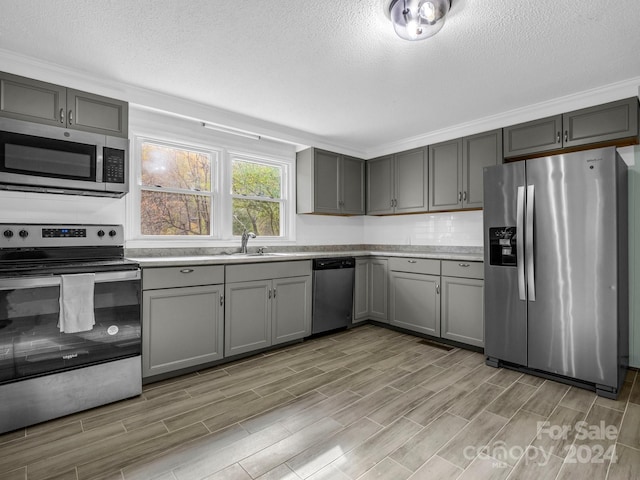 kitchen with a textured ceiling, gray cabinets, stainless steel appliances, and light hardwood / wood-style floors