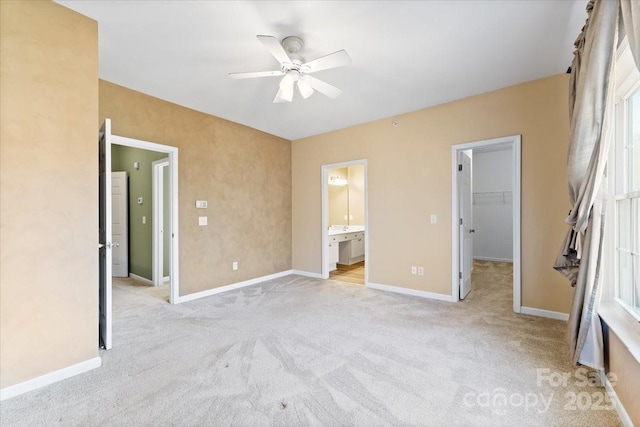 unfurnished bedroom with ensuite bathroom, a walk in closet, light colored carpet, a closet, and ceiling fan