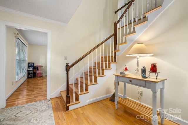 staircase with wood-type flooring, a textured ceiling, and crown molding