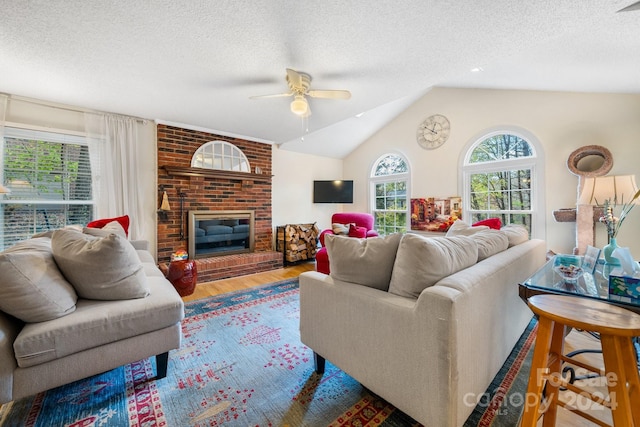 living room featuring a textured ceiling, hardwood / wood-style floors, vaulted ceiling, a brick fireplace, and ceiling fan