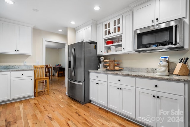 kitchen with white cabinets, light stone counters, light wood-type flooring, and appliances with stainless steel finishes