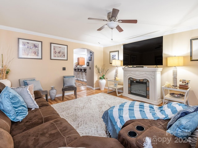 living room with a high end fireplace, light wood-type flooring, ceiling fan, and crown molding