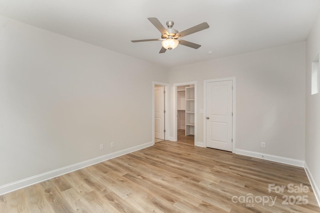 unfurnished bedroom featuring a walk in closet, light wood-style flooring, baseboards, and ceiling fan