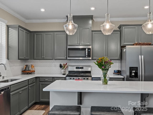 kitchen with appliances with stainless steel finishes, sink, hanging light fixtures, gray cabinets, and crown molding