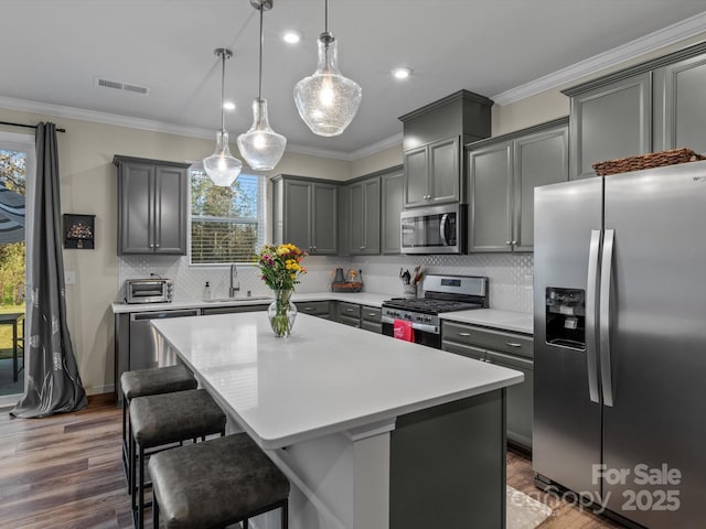 kitchen featuring a center island, stainless steel appliances, sink, hanging light fixtures, and crown molding