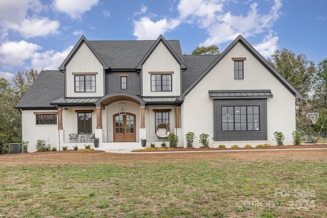 modern farmhouse style home featuring a front yard, cooling unit, covered porch, and french doors