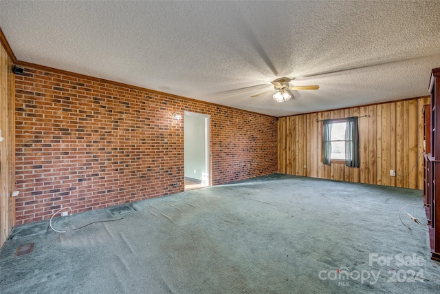 unfurnished room featuring carpet flooring, wood walls, a textured ceiling, and brick wall