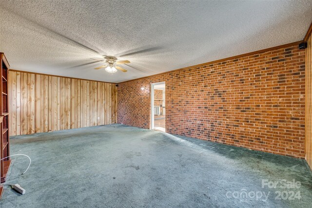 spare room with carpet, a textured ceiling, wooden walls, and brick wall