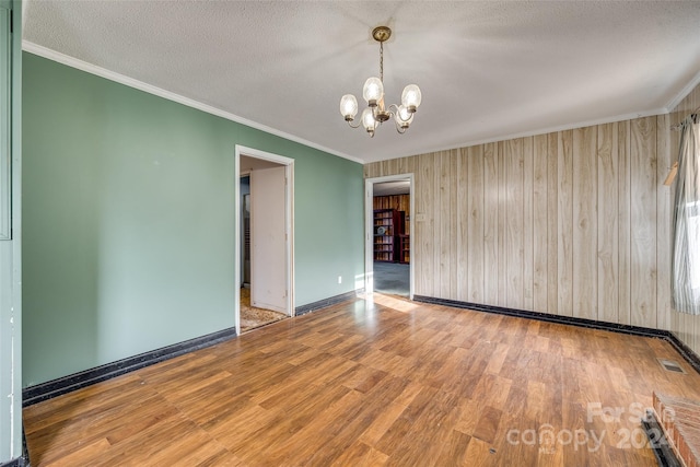 unfurnished room with a notable chandelier, wood walls, crown molding, wood-type flooring, and a textured ceiling