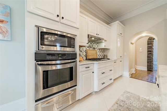 kitchen featuring light tile patterned flooring, white cabinetry, appliances with stainless steel finishes, tasteful backsplash, and crown molding