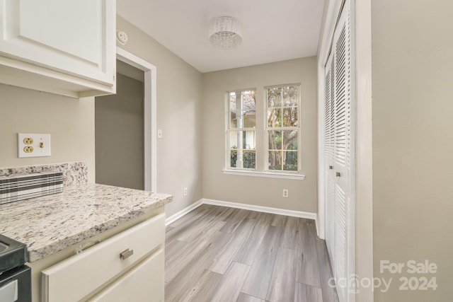 kitchen with white cabinetry, light wood-type flooring, and light stone counters