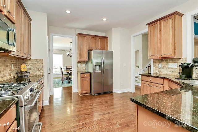 kitchen with dark stone countertops, decorative backsplash, light wood-type flooring, and appliances with stainless steel finishes