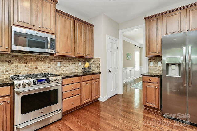 kitchen with dark hardwood / wood-style flooring, dark stone counters, backsplash, and stainless steel appliances