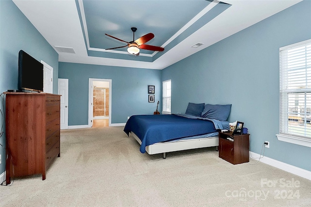 bedroom featuring light colored carpet, a raised ceiling, ceiling fan, and ensuite bath