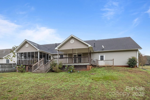 back of property with a wooden deck, a sunroom, and a lawn