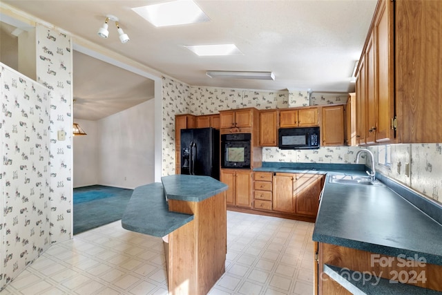 kitchen featuring black appliances, sink, lofted ceiling with skylight, and a breakfast bar area