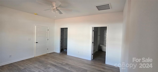 unfurnished bedroom with a walk in closet, hardwood / wood-style flooring, ensuite bath, and ceiling fan